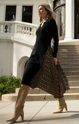 Woman in a black cardigan and patterned skirt standing on steps in front of a building.