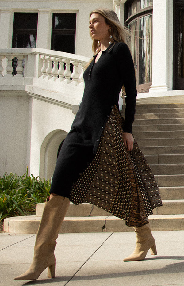 Woman in a black cardigan and patterned skirt standing on steps in front of a building.